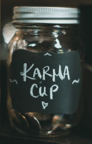 A charming glass jar labeled 'Karma Cup' filled with coins on a rustic wooden shelf.